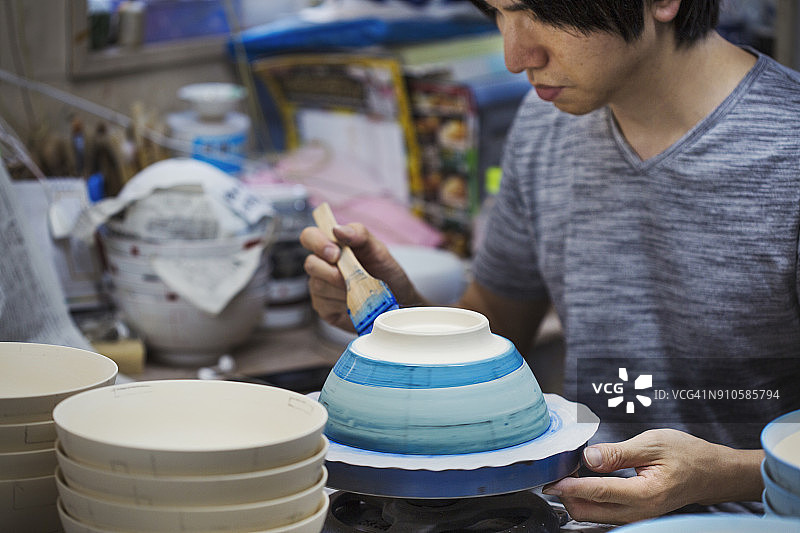 男人在日本瓷器作坊工作，用蓝色釉料绘制白色碗的特写图片素材