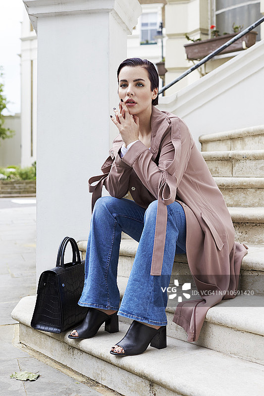 穿着外套和牛仔裤坐在房子外台阶上的女人图片素材