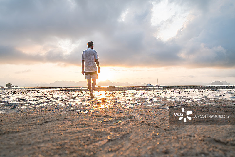 年轻男子在日出时分走在沙滩上的背影图片素材