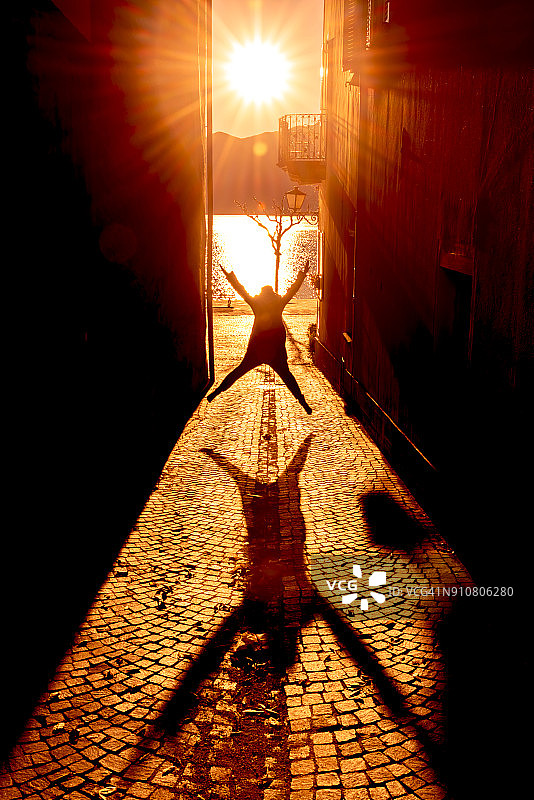 阳光下在狭窄街道上跳跃的快乐女人图片素材