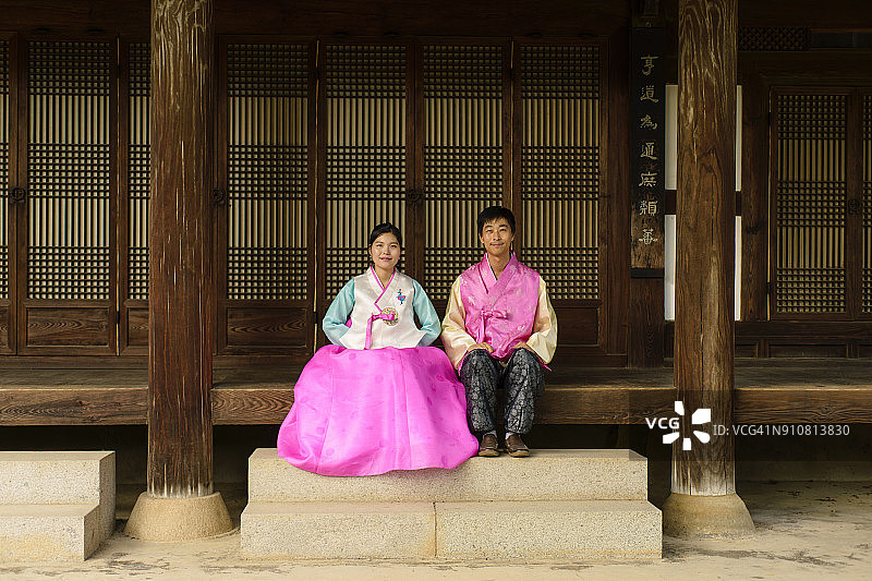 身穿韩国传统服装的情侣在木制门廊上的场景图片素材
