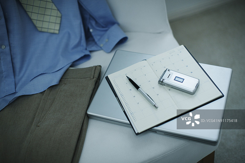 沙发上的手机、笔记本、钢笔、笔记本电脑、衬衫、领带和裤子图片素材