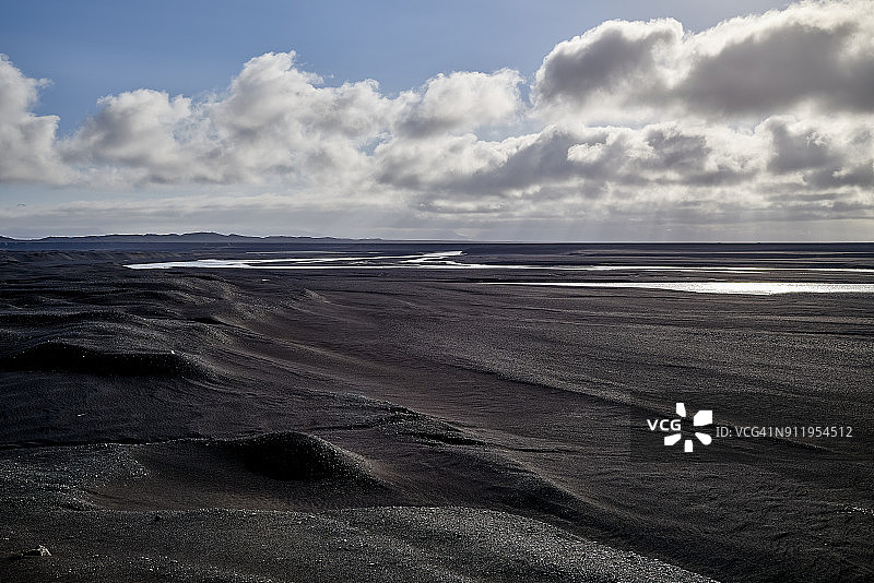 河流流经黑色沙滩河床，远处是群山图片素材