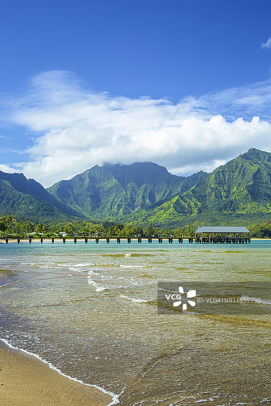 通往海边的码头，海浪拍打着沙滩，背景是崎岖的绿色山脉图片素材