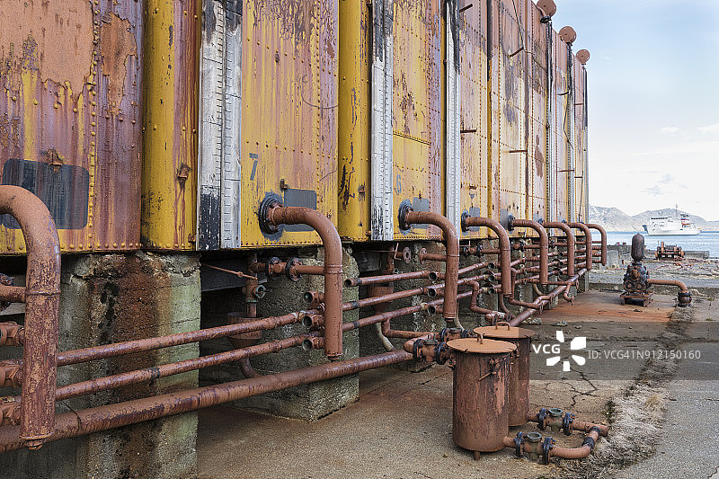 南乔治亚岛格里特维肯废弃捕鲸站的废弃鲸油加工设备，后方海湾有游览船图片素材