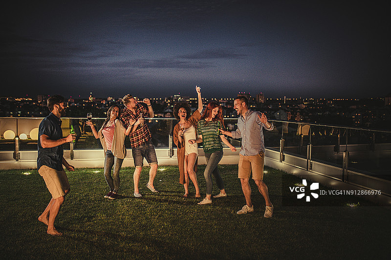 一群快乐的朋友在顶层公寓露台的夜间派对上跳舞唱歌图片素材