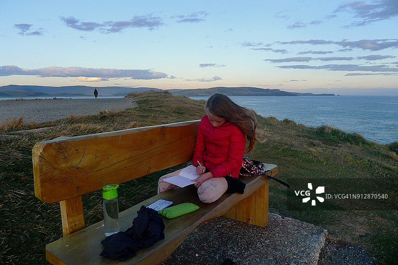 日落时分在库里奥湾悬崖顶的长椅上绘画和休息的女孩图片素材