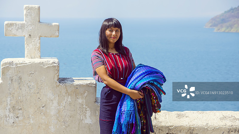 年轻的玛雅妇女在危地马拉阿蒂特兰湖岸边 carrying 出售的编织图案桌布图片素材