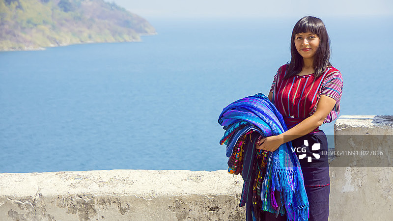 年轻的玛雅妇女在危地马拉阿蒂特兰湖岸边 carrying 出售的编织图案桌布图片素材