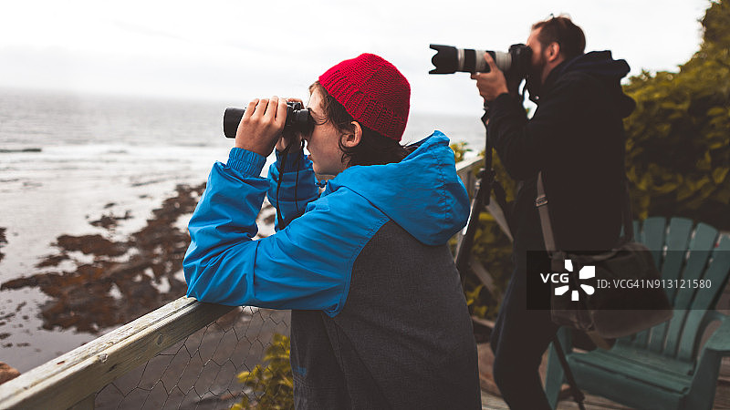 父亲用长焦镜头拍照，儿子用望远镜观海，加拿大魁北克图片素材