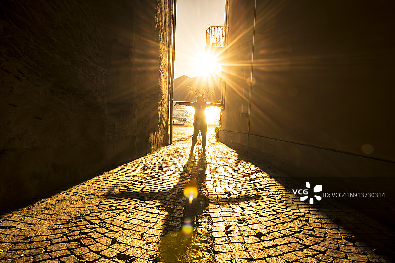 阳光和阴影照射下，张开双臂的女人在狭窄的街道上图片素材