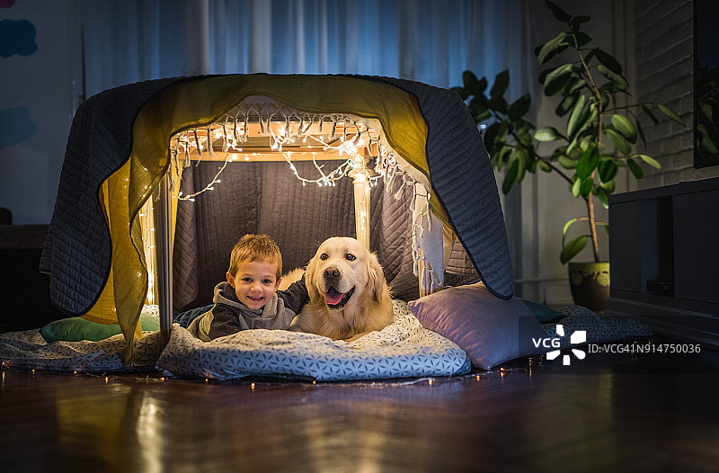 快乐的小男孩在家里的帐篷里拥抱他的狗图片素材