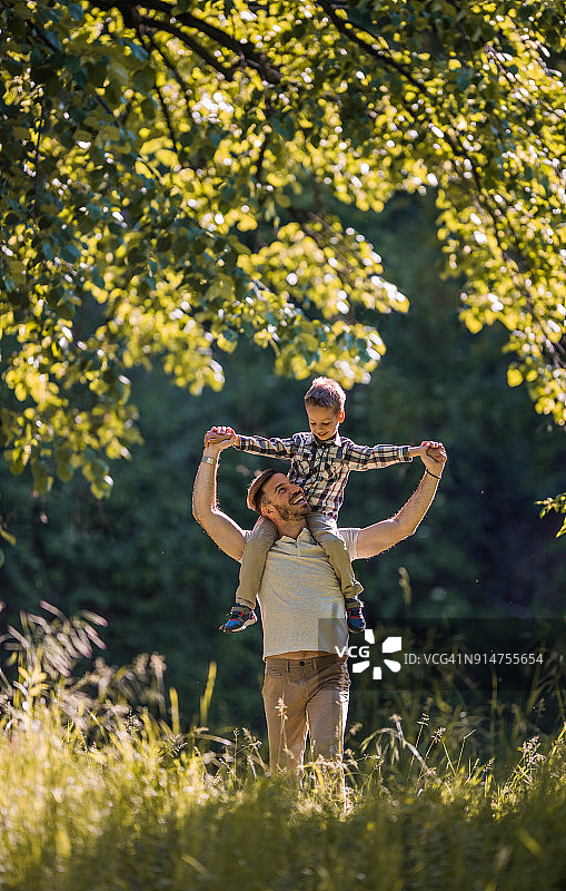 快乐的父亲在春日公园里把儿子扛在肩上图片素材