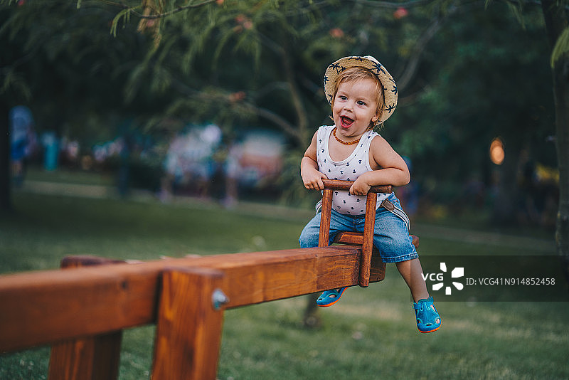 快乐的小男孩在公园里玩跷跷板图片素材