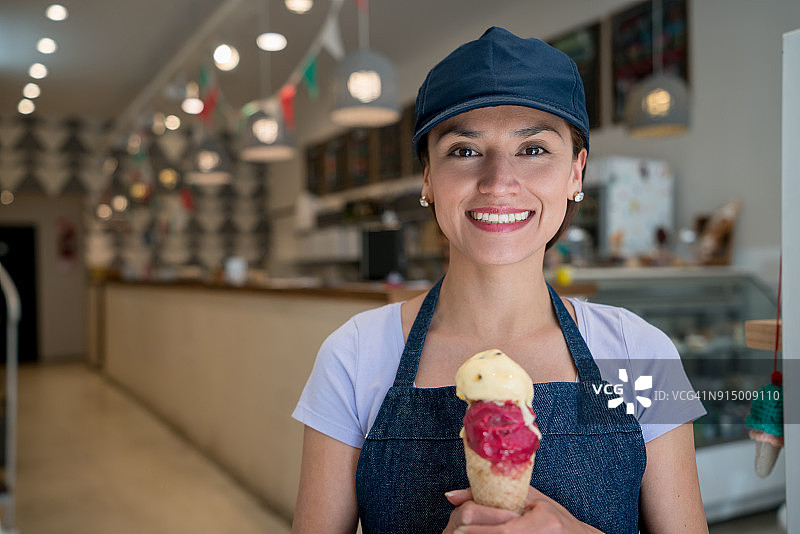 在冰淇淋店拿着冰淇淋筒微笑看着镜头的漂亮女售货员图片素材