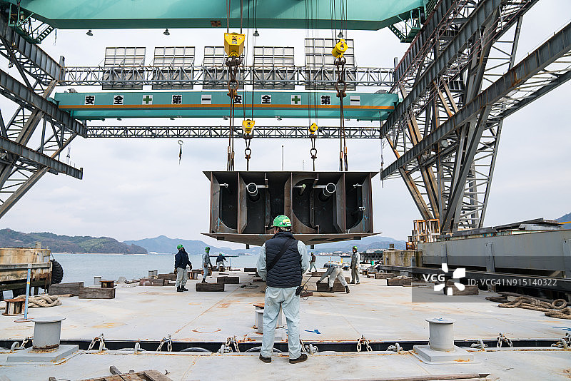 远程起重机操作员将大型船只部件吊到驳船上图片素材