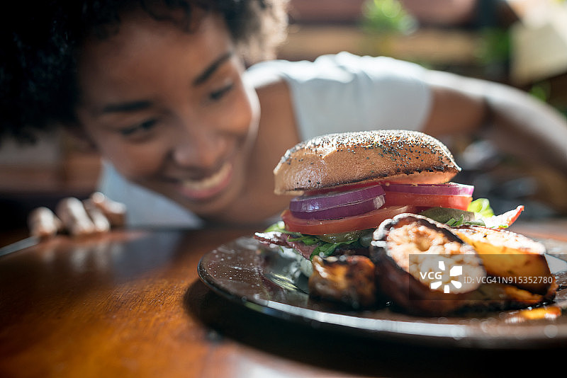 年轻的非洲裔美国女性看着她的汉堡，靠在桌子上图片素材