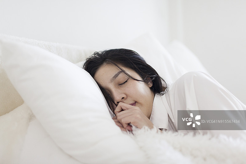 穿白色连衣裙的亚洲女孩在舒适卧室睡觉图片素材