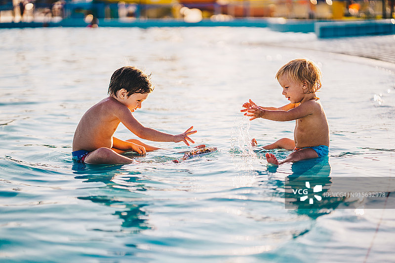 无忧无虑的男孩在游泳池里玩玩具船图片素材
