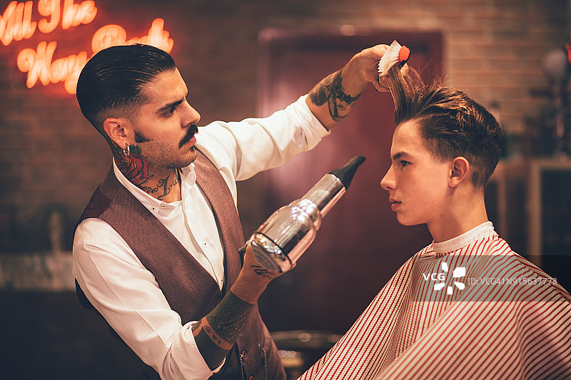 年轻时尚的美发师为时髦男士吹干头发图片素材