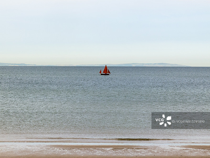 康威沙滩附近海面上的红色帆船：威尔士海岸小径-北威尔士图片素材