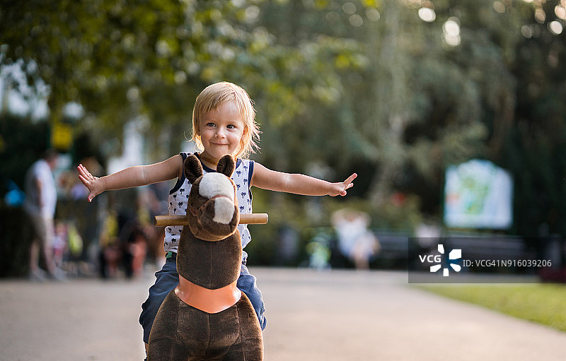 张开双臂骑着玩具马的快乐男孩图片素材