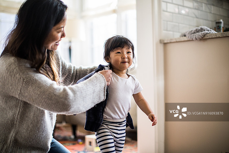 母亲帮助女儿（2岁）穿外套图片素材
