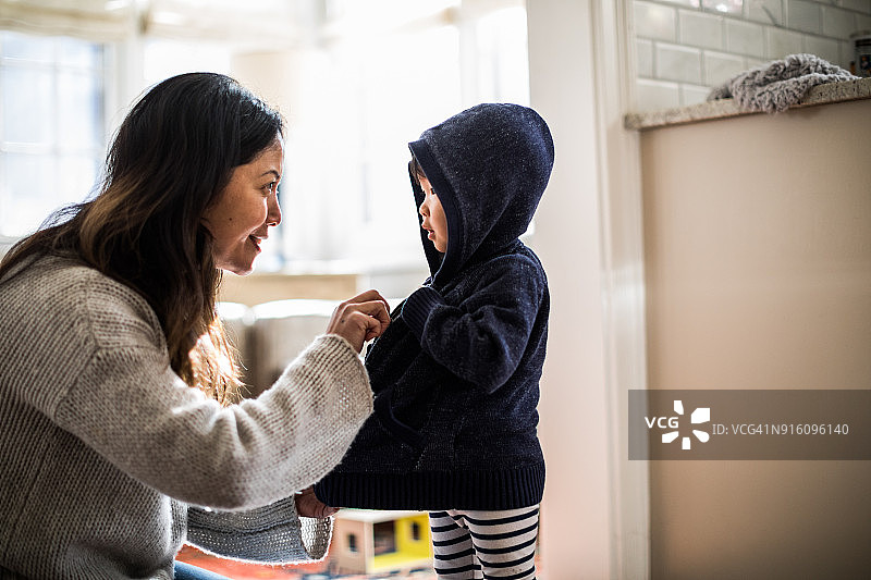 母亲帮助女儿（2岁）穿外套图片素材