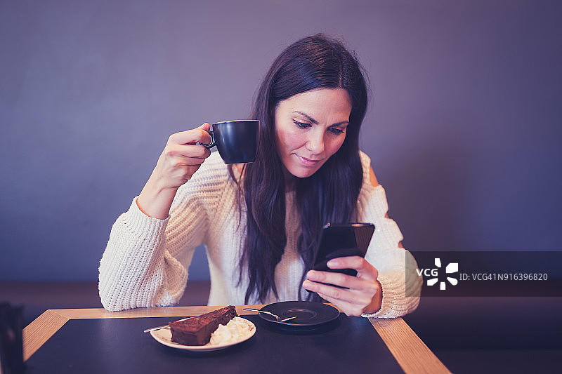 年轻女人在咖啡馆里喝咖啡，使用智能手机图片素材