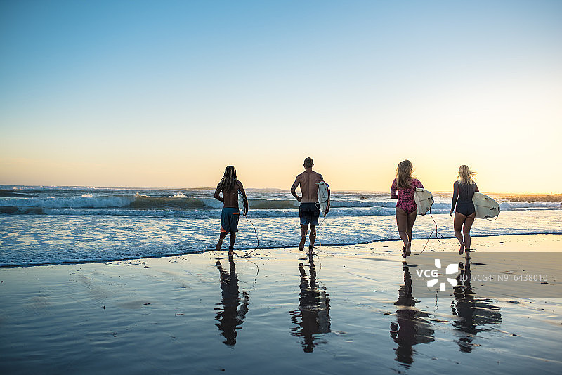 四位朋友站在海滩上，拿着冲浪板图片素材