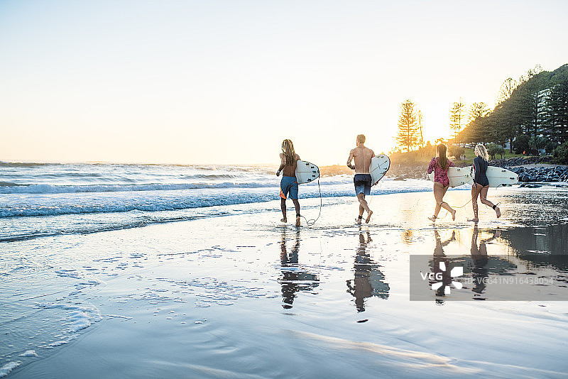 朋友们日落时分带着冲浪板奔向水中图片素材