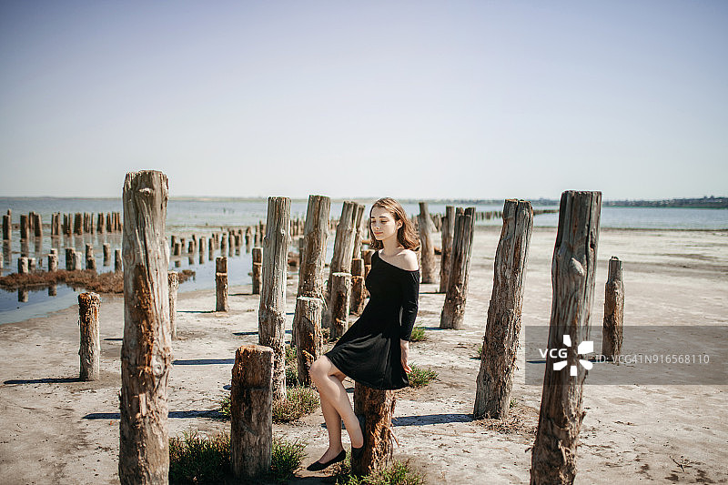 悲伤的年轻女子坐在木制防波堤柱子上图片素材