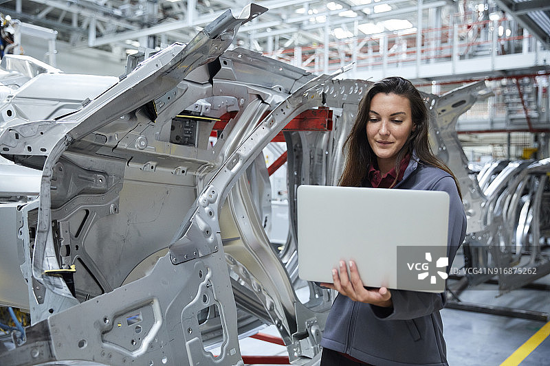 工程师在工厂里靠汽车底盘使用笔记本电脑图片素材