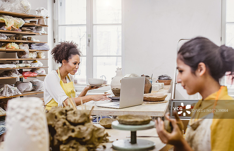手持陶艺品、看笔记本电脑的女人图片素材