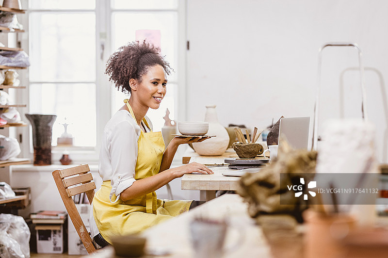 手持陶艺品、看笔记本电脑的女人图片素材