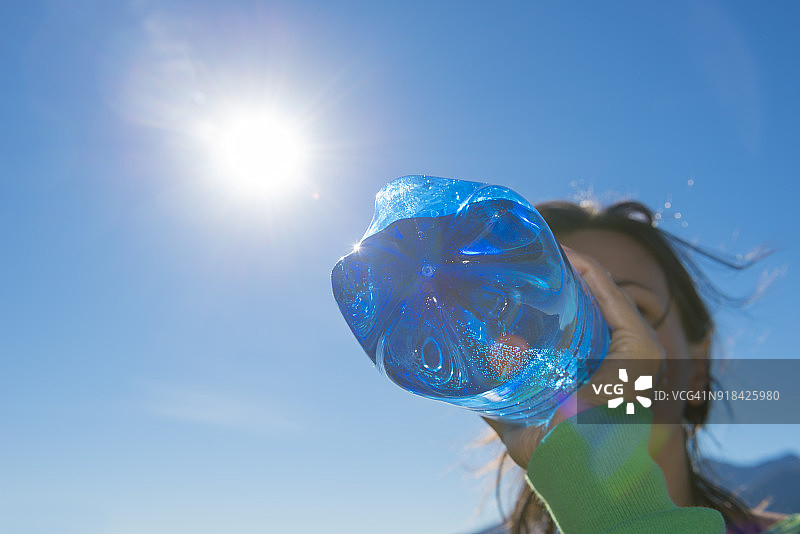阳光下，女人喝蓝色瓶装水图片素材