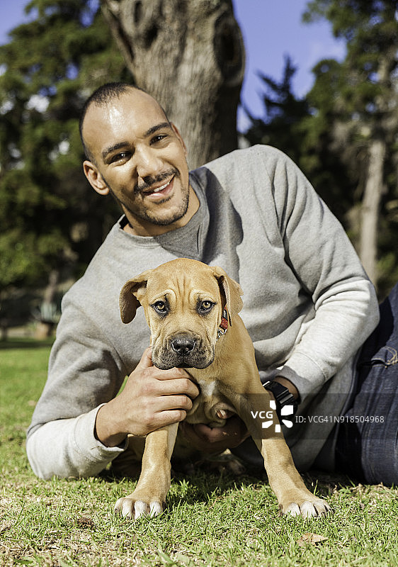 年轻男人和他的小狗在公园的草地上图片素材