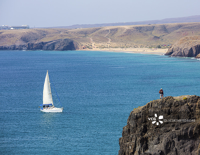 情侣站在兰萨罗特岛帕帕加约海滩的悬崖顶上，游艇驶近图片素材