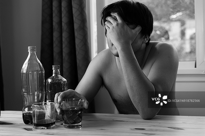 疲惫的亚洲男人手扶头部，喝着酒图片素材