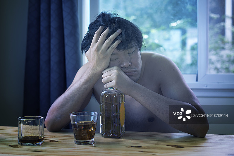 疲惫的亚洲男人手扶头部，喝着酒图片素材