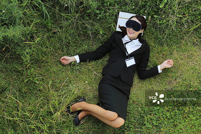 戴着睡眠眼罩在草地上放松的商务女人图片素材