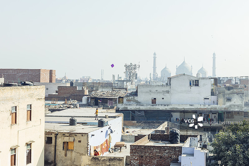 在远处有寺庙的旧德里上空，一个男孩在放紫色的风筝图片素材