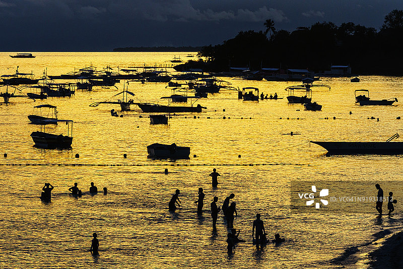 菲律宾薄荷岛邦劳海滩沐浴在金色光芒中的大海和船只以及傍晚的沐浴者图片素材