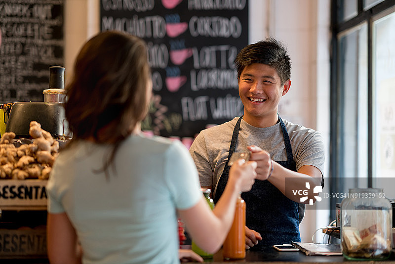 女顾客在果汁吧用信用卡支付果汁，男销售员结账图片素材