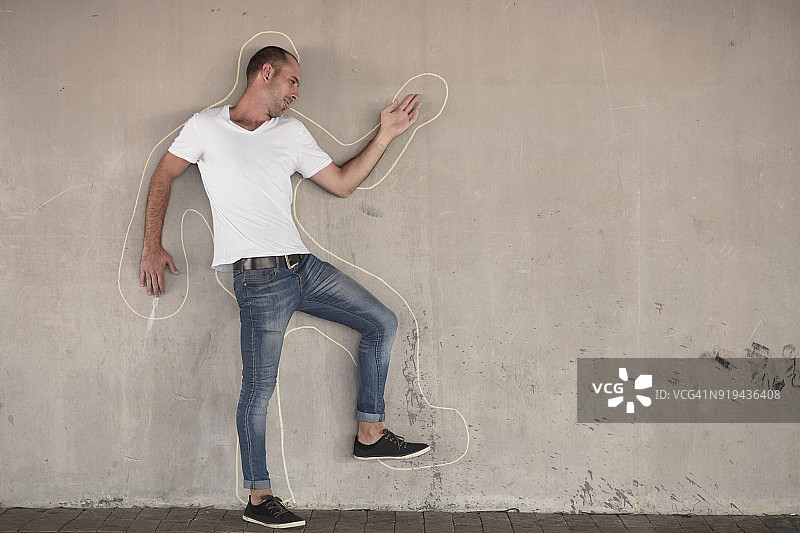 男人假装死亡，站在混凝土墙上用粉笔画出的轮廓旁图片素材