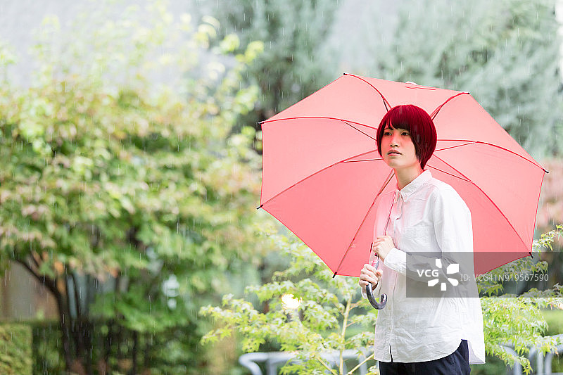 在办公楼花园里打着红色雨伞的亚洲女性图片素材