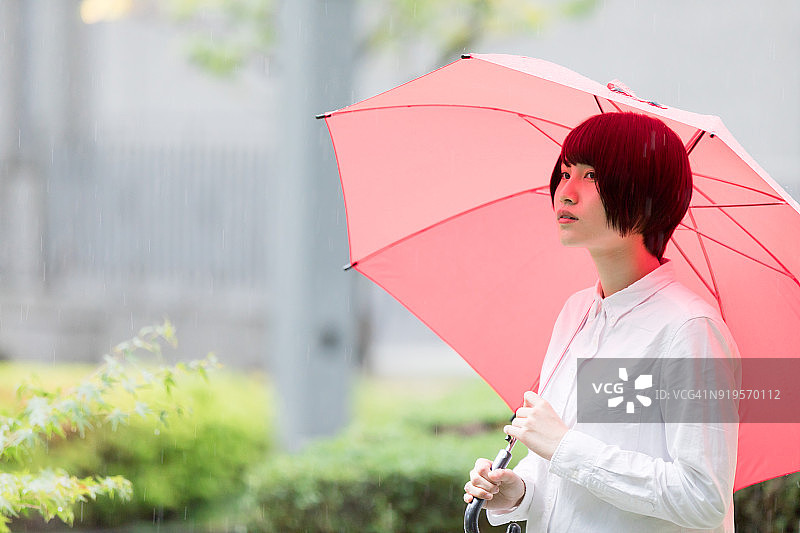 在办公楼花园里打着红色雨伞的亚洲女性图片素材