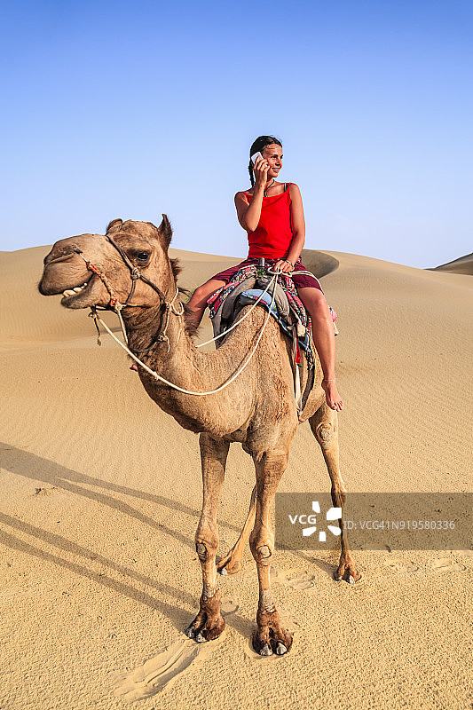 年轻女游客在印度拉贾斯坦邦骑骆驼使用手机图片素材