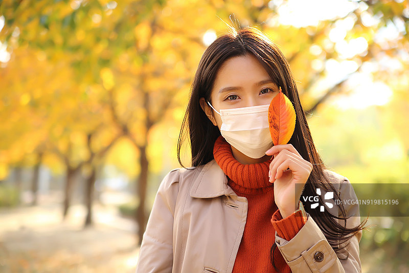 戴口罩在公园拿树叶的女人图片素材