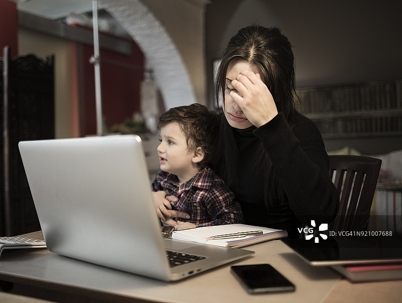 在家工作并抱着哭泣小儿子的焦虑女人图片素材